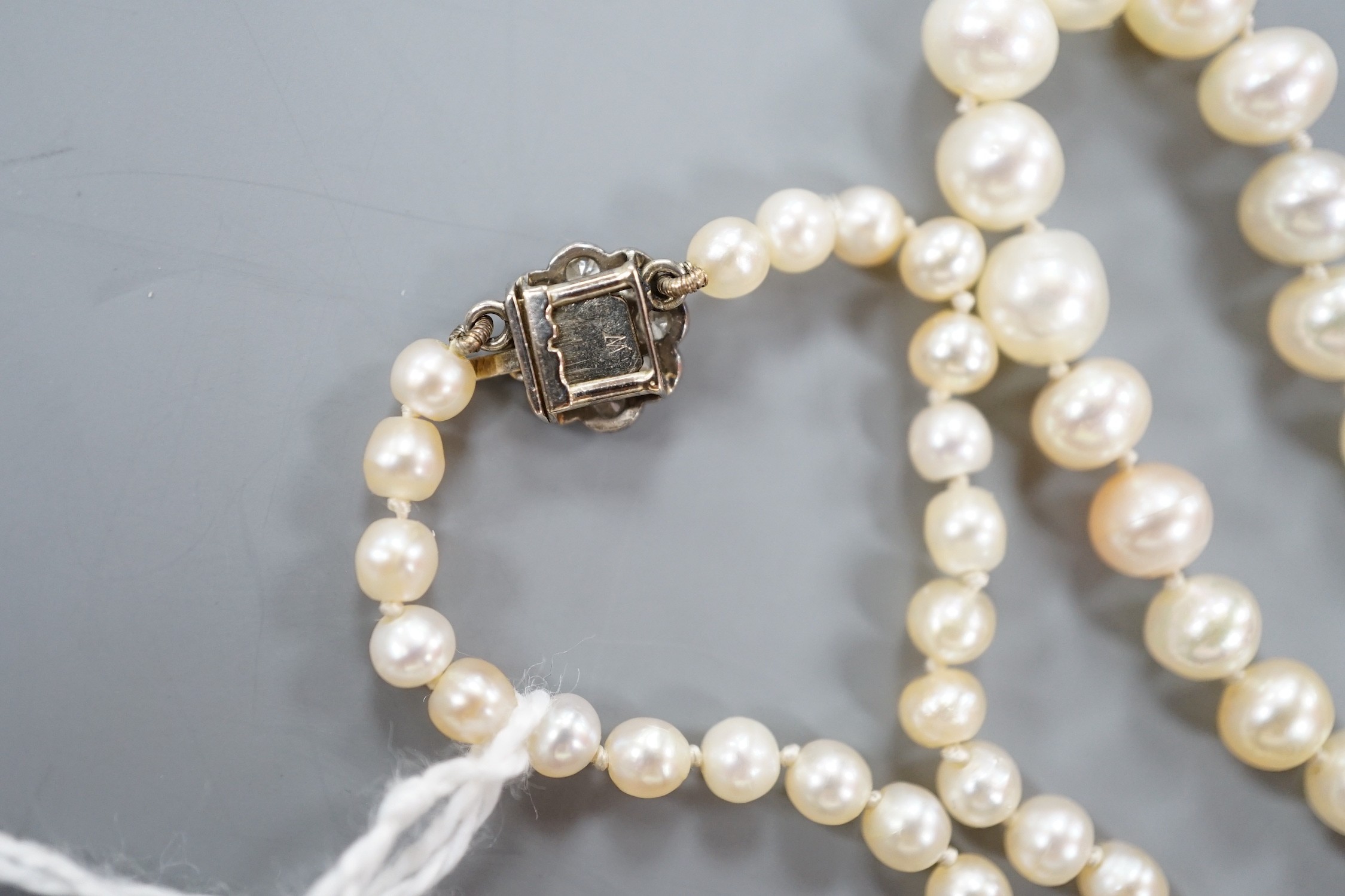 An early 20th century single strand possibly part natural? and part cultured pearl necklace, with diamond cluster set white metal clasp, 112cm.